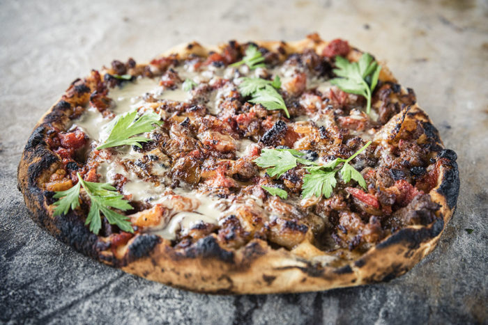 Closeup of baked sficha with charred crust on the edges, garnished with parsley, and beautifully presented on a dusted surface.